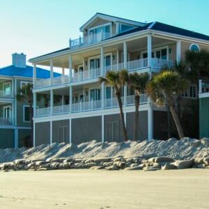 Contemporary beachfront villas with palm trees lining the sandy shore under a clear sky.